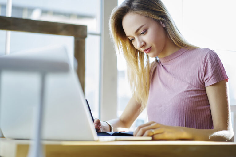 Concentrated blonde female student writing report doing homework